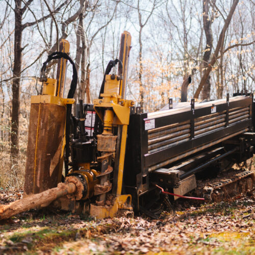 Drilling machine bores underground in a wooded area.