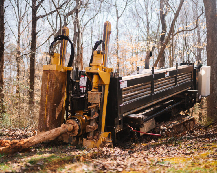 Drilling machine bores underground in a wooded area.