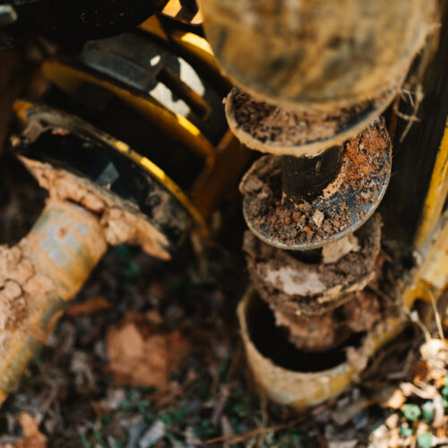 Muddy auger drill bit on machinery, used for ground drilling.