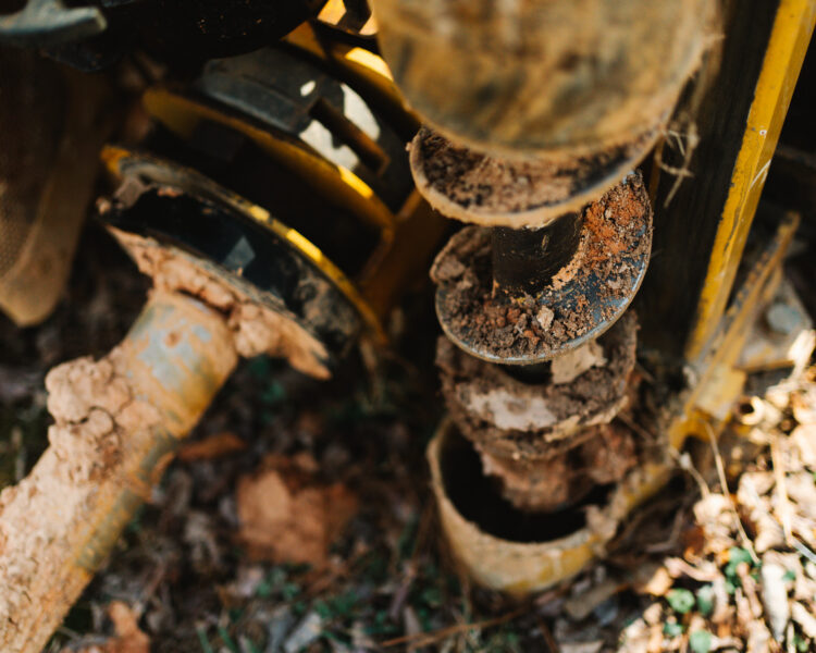 Muddy auger drill bit on machinery, used for ground drilling.