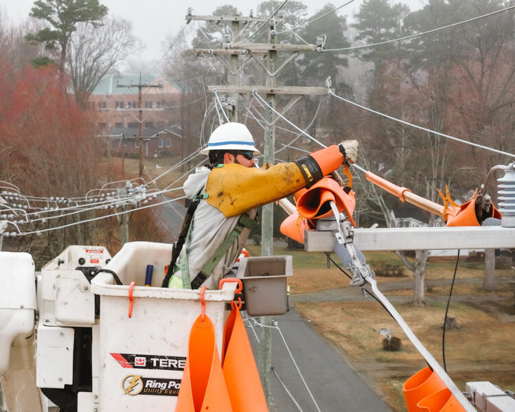 Utility worker in bucket truck covers power lines with orange sleeves.