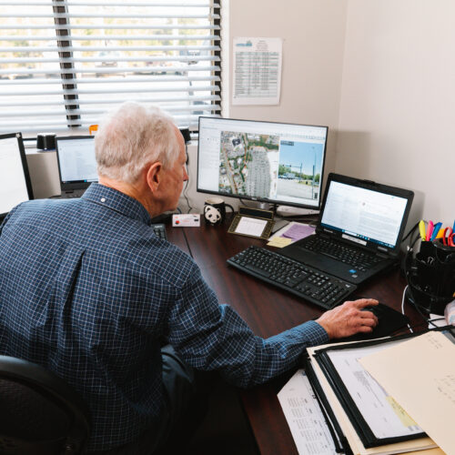Older man works at desk with monitors and papers.