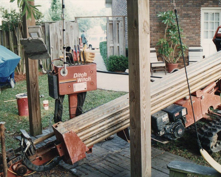 Ditch Witch machine in backyard, pipes and tools nearby.