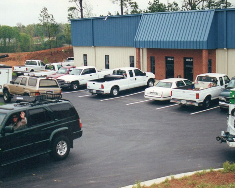 Cars and trucks in parking lot; person waves from dark green SUV.