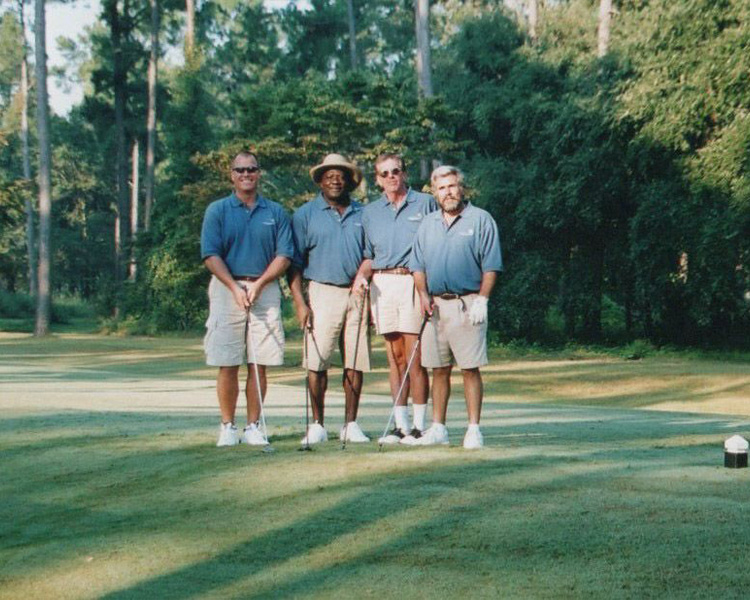 Four men in blue shirts and khakis on a golf course.