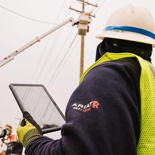 Utility worker with tablet watches colleague on bucket truck.