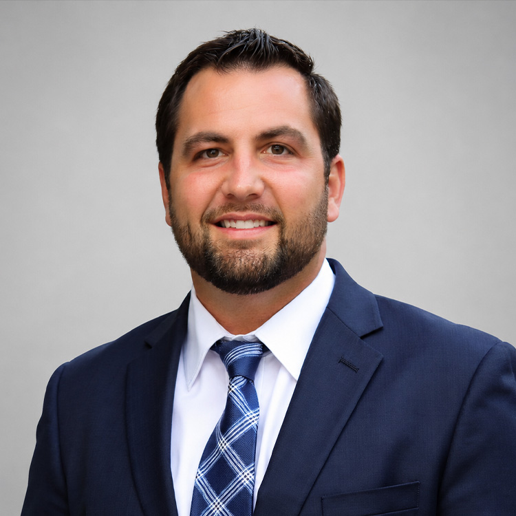 Smiling man in blue suit and white shirt on gray background.