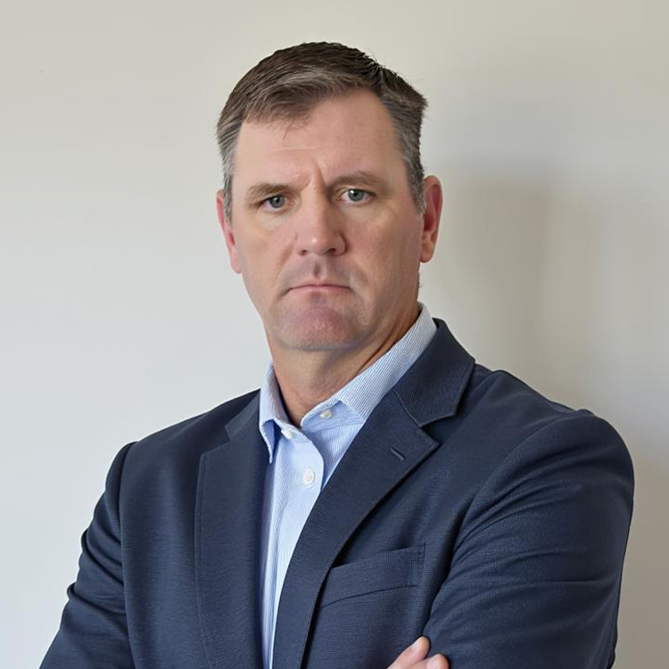 Man in navy blazer with arms crossed against plain background.