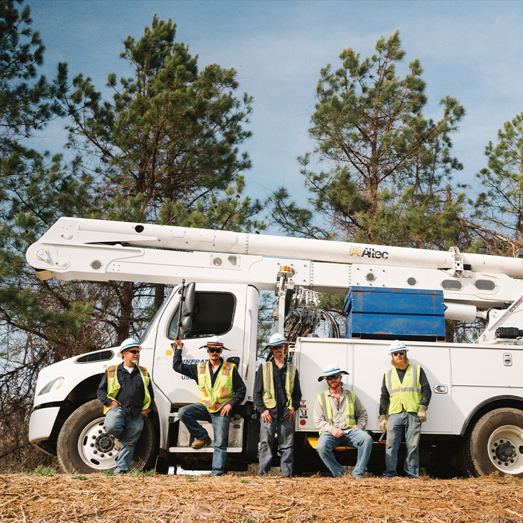 Workers in safety vests stand by a utility truck outdoors.