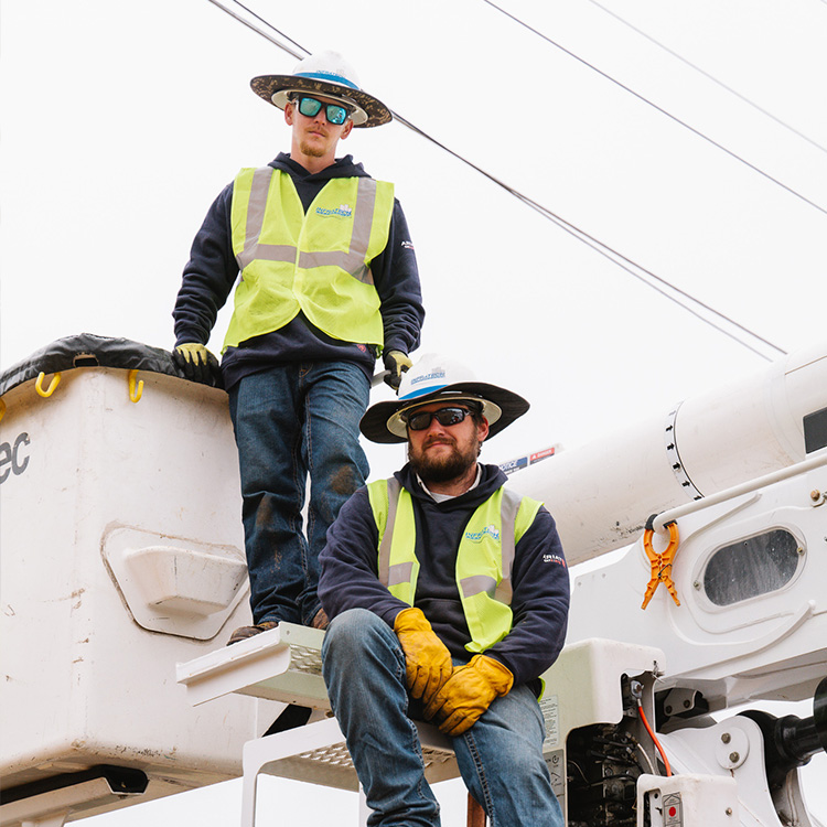 Utility workers by a bucket truck with visible power lines.