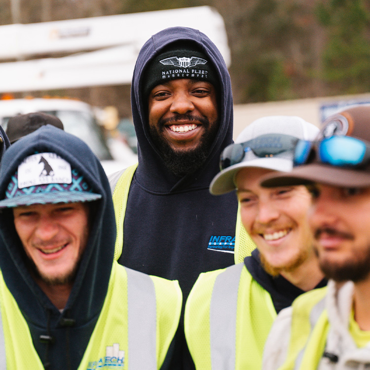 Four smiling construction workers in safety gear by a utility truck.