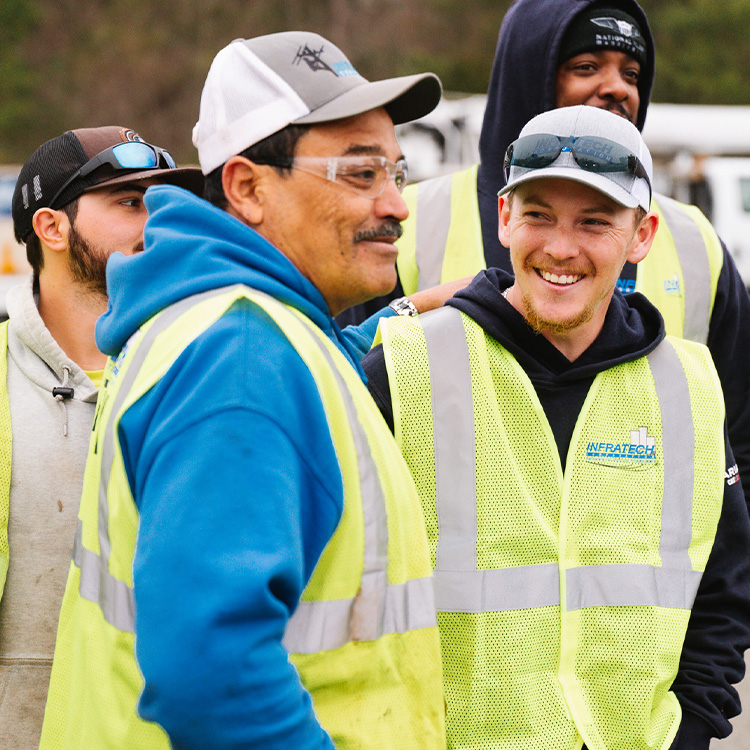 Construction workers in safety gear stand outdoors, some smiling.