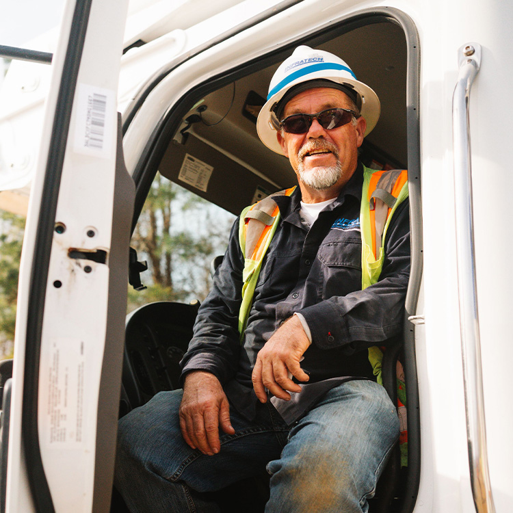 Construction worker in vest and helmet sits in white utility vehicle.