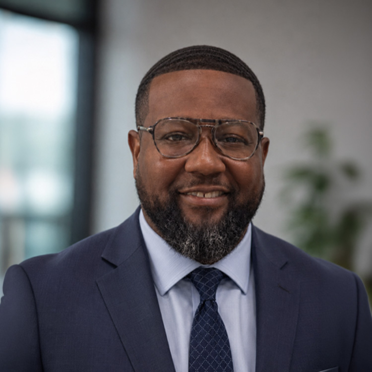 Man in glasses and navy suit smiles indoors.
