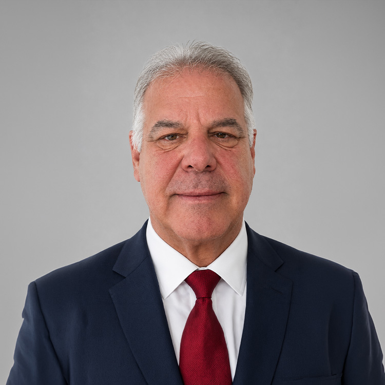 Gray-haired man in blue suit and red tie on gray background.