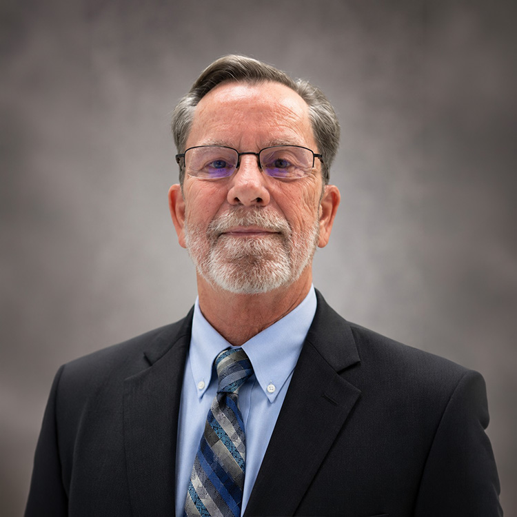 Older man in suit and tie poses against gray background.