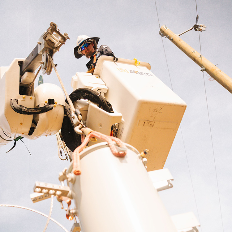 Utility worker in safety gear using bucket truck by power lines.