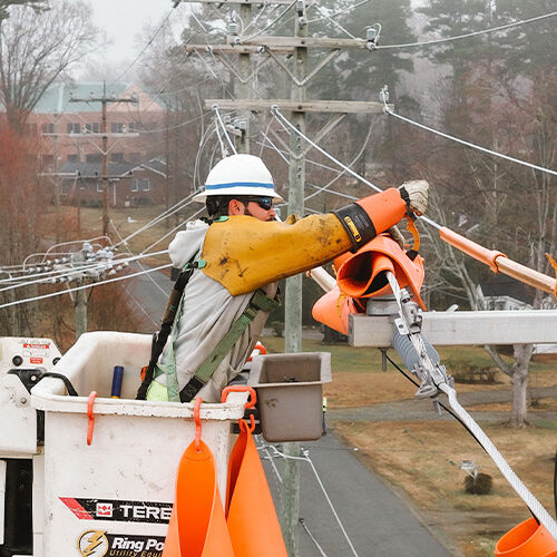 Utility worker in bucket truck placing covers on power lines.