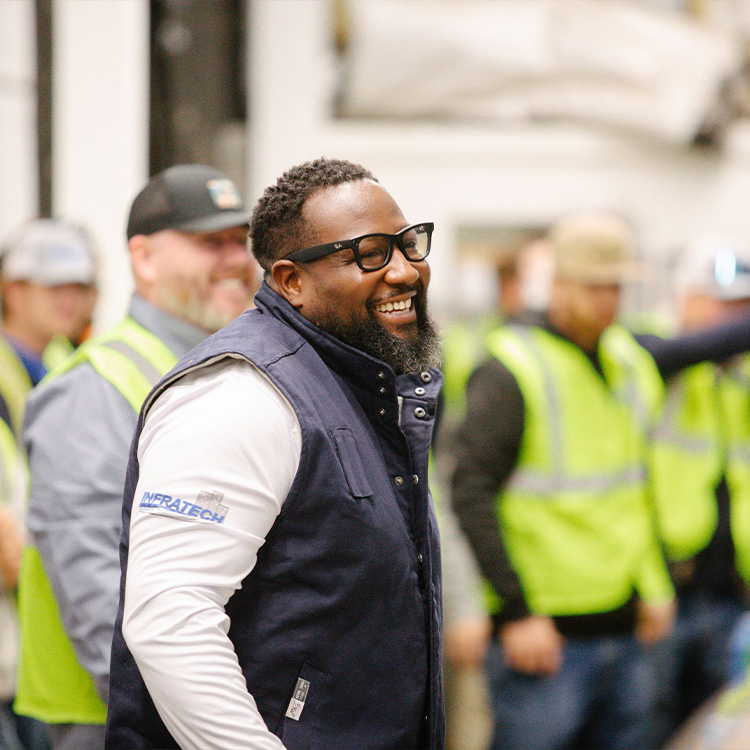 Smiling man in glasses, with blurred people in safety vests behind.