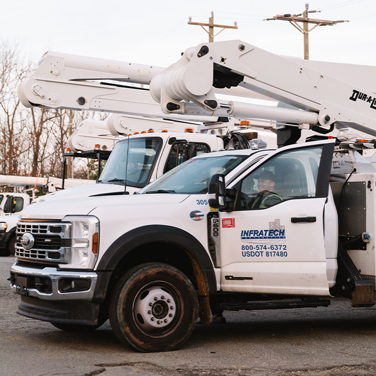 White Infratech utility truck with boom, worker inside, power lines.