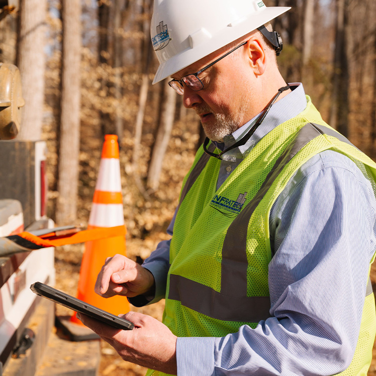Construction worker with hard hat uses tablet at job site.