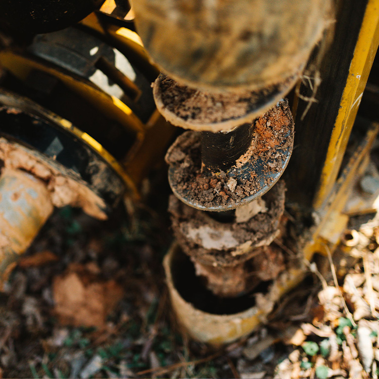 Dirt-covered auger drill bit on yellow machinery.