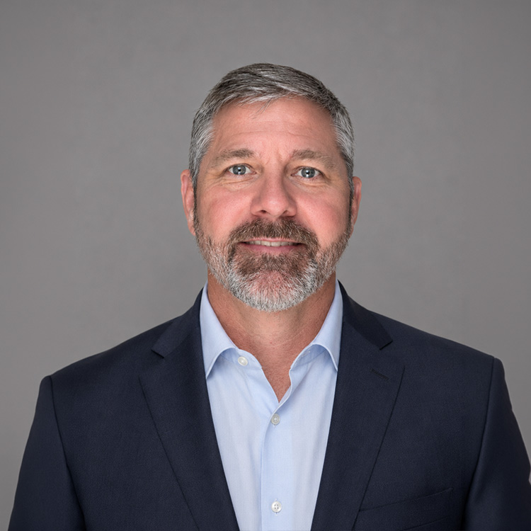Middle-aged man with gray hair, beard, suit jacket, blue shirt.