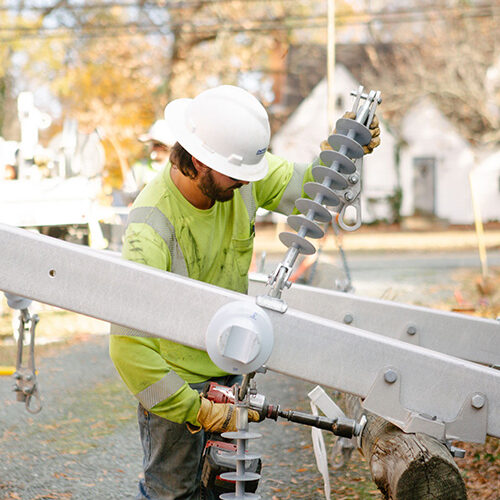 Worker in hard hat repairs electrical equipment outside homes.